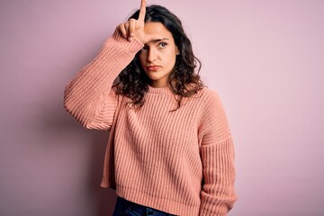 Young beautiful woman with curly hair wearing casual sweater over isolated pink background making...