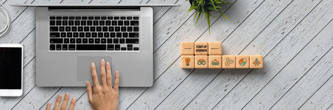 cubes with German message for FOUND A START-UP and tech icons with office equipment on wooden background