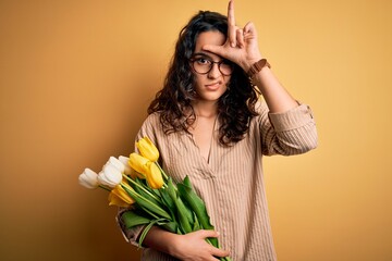 Young beautiful romantic woman with curly hair holding bouquet of yellow tulips making fun of...