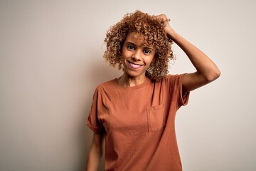 Beautiful african american woman with curly hair wearing casual t-shirt over white background confuse and wonder about question. Uncertain with doubt, thinking with hand on head. Pensive concept.