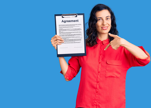 Young beautiful hispanic woman holding clipboard with agreement document pointing finger to one self smiling happy and proud