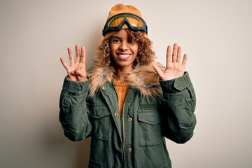 Young african american skier woman with curly hair wearing snow sportswear and ski goggles showing and pointing up with fingers number nine while smiling confident and happy.