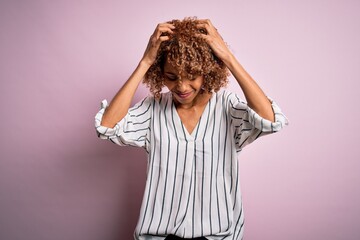 Fototapeta na wymiar Beautiful african american woman with curly hair wearing striped t-shirt over pink background suffering from headache desperate and stressed because pain and migraine. Hands on head.