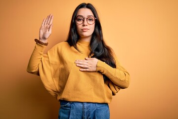 Young brunette woman wearing glasses and casual sweater over yellow isolated background Swearing...