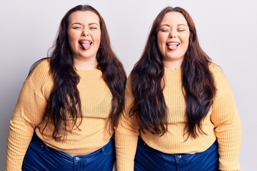 Young plus size twins wearing casual clothes sticking tongue out happy with funny expression. emotion concept.