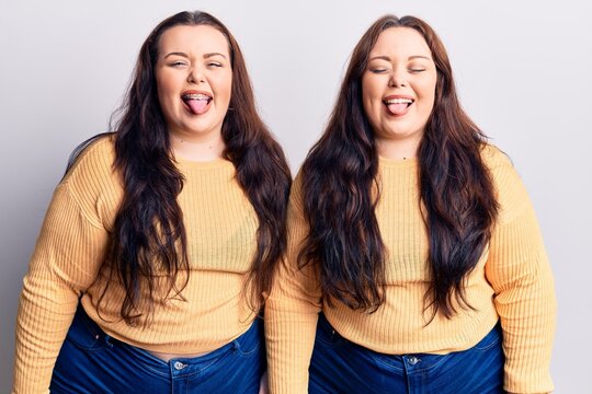Young plus size twins wearing casual clothes sticking tongue out happy with funny expression. emotion concept.