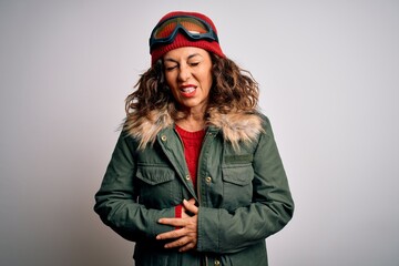 Middle age skier woman wearing snow sportswear and ski goggles over white background with hand on stomach because indigestion, painful illness feeling unwell. Ache concept.