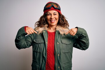 Middle age skier woman wearing snow sportswear and ski goggles over white background looking confident with smile on face, pointing oneself with fingers proud and happy.