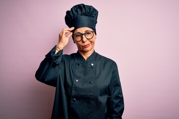 Middle age brunette chef woman wearing cooker uniform and hat over isolated pink background worried and stressed about a problem with hand on forehead, nervous and anxious for crisis