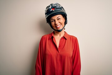 Middle age motorcyclist woman wearing motorcycle helmet over isolated white background winking looking at the camera with sexy expression, cheerful and happy face.