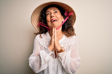 Middle age brunette woman wearing asian traditional conical hat over white background begging and praying with hands together with hope expression on face very emotional and worried. Begging.