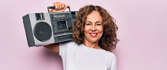 Middle age brunette hipster woman holding retro music boombox over pink isolated background looking positive and happy standing and smiling with a confident smile showing teeth