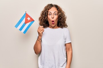 Middle age beautiful tourist woman holding cuban flag over isolated white background scared and amazed with open mouth for surprise, disbelief face