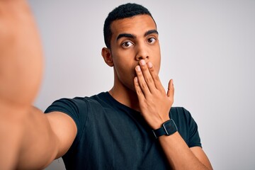 Young handsome african american man wearing casual t-shirt making selfie by camera cover mouth with...