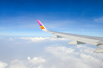 Fototapeta premium A wing of plane in the sky. Beautiful view of blue sky above the white clouds from airplane window.