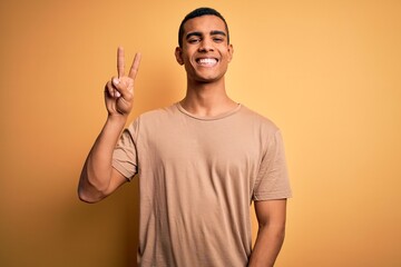 Young handsome african american man wearing casual t-shirt standing over yellow background showing and pointing up with fingers number two while smiling confident and happy.
