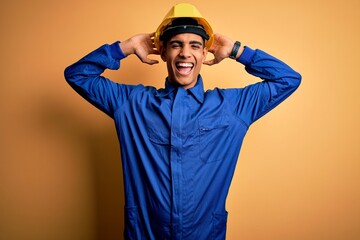 Young handsome african american worker man wearing blue uniform and security helmet relaxing and...