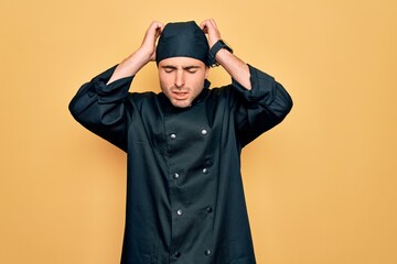 Young handsome cooker man with blue eyes wearing uniform and hat over yellow background suffering from headache desperate and stressed because pain and migraine. Hands on head.