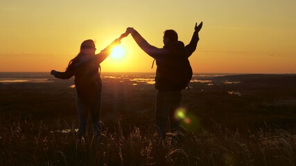 Fototapeta na wymiar Travelers, man and woman with backpack, go to edge of hill in rays of dawn, raise their hands, clap their hands and enjoy victory and beautiful sun and landscape. family travel and tourism concept