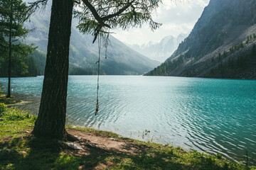 Atmospheric idyllic landscape with rope swing on tree near alpine lake with relax waves on...