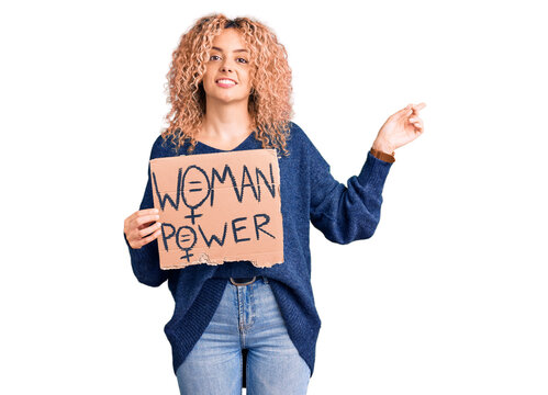 Young blonde woman with curly hair holding we need a change banner smiling happy pointing with hand and finger to the side