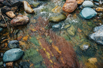 Scenic landscape with awesome motley small river. Picturesque view to beautiful mountain creek with multicolor clay on bottom. Amazing vivid scenery with mountain stream. Nature background with brook.