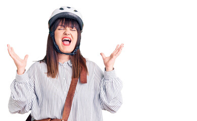 Young plus size woman wearing bike helmet and leather bag celebrating mad and crazy for success with arms raised and closed eyes screaming excited. winner concept