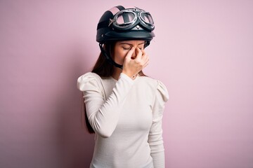 Young beautiful motorcyclist woman with blue eyes wearing moto helmet over pink background tired rubbing nose and eyes feeling fatigue and headache. Stress and frustration concept.