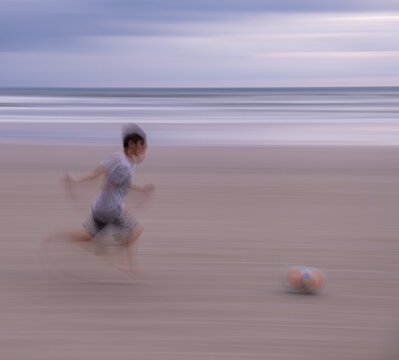 imagem em movimento desfocada de garoto correndo na praia com bola de futebol