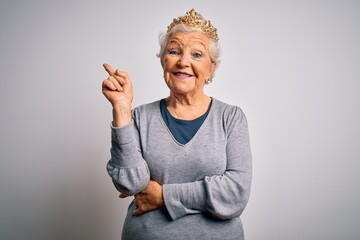 Senior beautiful grey-haired woman wearing golden queen crown over white background with a big...