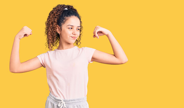 Beautiful kid girl with curly hair wearing casual clothes showing arms muscles smiling proud. fitness concept.