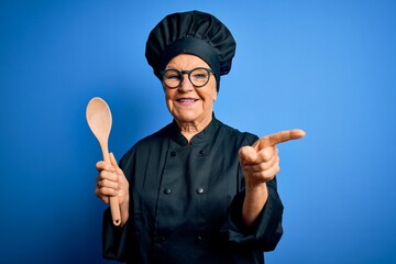 Senior beautiful grey-haired chef woman wearing cooker uniform and hat holding wooden spoon very...