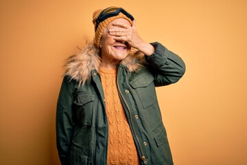 Senior beautiful grey-haired skier woman wearing snow sportswear and ski goggles smiling and laughing with hand on face covering eyes for surprise. Blind concept.