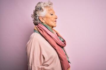 Fototapeta premium Senior beautiful grey-haired woman wearing casual sweater and scarf over pink background looking to side, relax profile pose with natural face with confident smile.