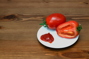 Tomato and sliced red tomato on a white plate with ketchup on the background of a wooden table.