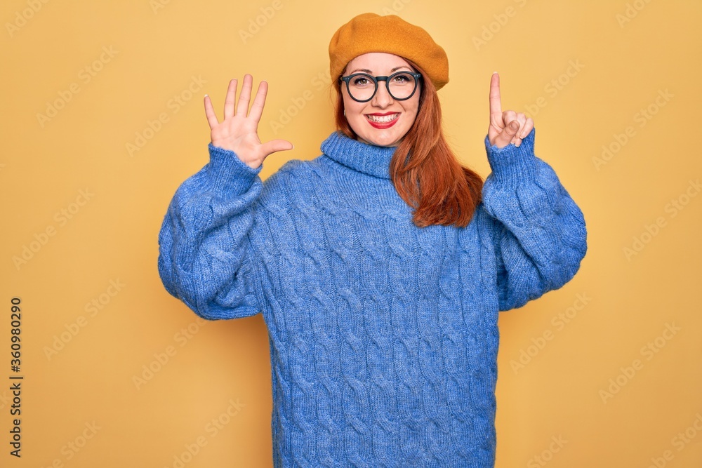 Canvas Prints Young beautiful redhead woman wearing french beret and glasses over yellow background showing and pointing up with fingers number six while smiling confident and happy.