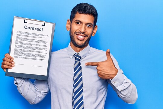 Young latin man holding clipboard with contract document pointing finger to one self smiling happy and proud