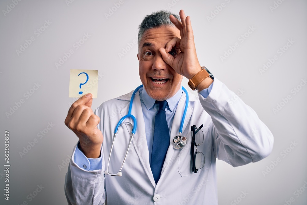 Canvas Prints Middle age handsome grey-haired doctor man holding paper with question mark with happy face smiling doing ok sign with hand on eye looking through fingers