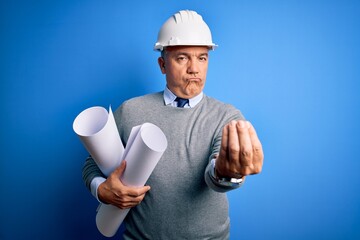 Middle age handsome grey-haired architect man wearing safety helmet holding blueprints doing money gesture with hands, asking for salary payment, millionaire business