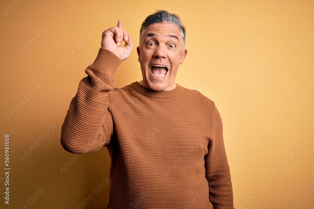 Sticker middle age handsome grey-haired man wearing casual sweater over yellow background pointing finger up