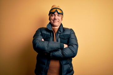 Middle age handsome grey-haired skier man on vacation wearing ski goggles happy face smiling with crossed arms looking at the camera. Positive person.