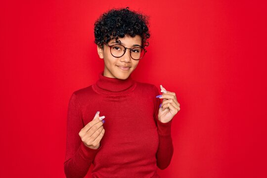 Young beautiful african american afro woman wearing turtleneck sweater and glasses doing money gesture with hands, asking for salary payment, millionaire business