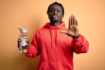Young african american sporty man wearing sweatshirt with hoodie drinking bottle of water with open...