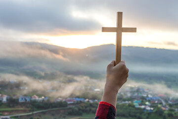 Human praying to the GOD while holding a crucifix symbol with bright sunbeam on the sky