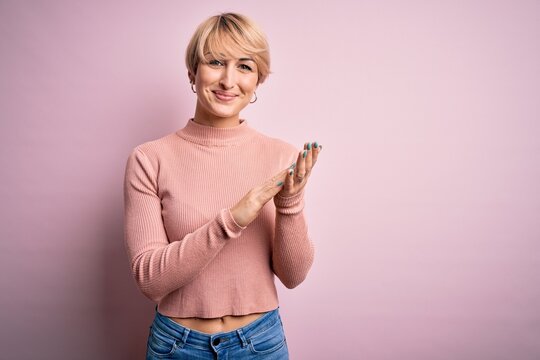Young blonde woman with short hair wearing casual turtleneck sweater over pink background clapping and applauding happy and joyful, smiling proud hands together