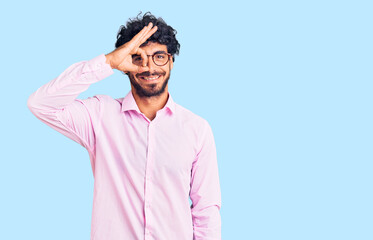 Handsome young man with curly hair and bear wearing business clothes doing ok gesture with hand smiling, eye looking through fingers with happy face.