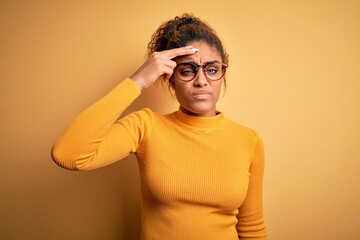 Young beautiful african american girl wearing sweater and glasses over yellow background worried and stressed about a problem with hand on forehead, nervous and anxious for crisis