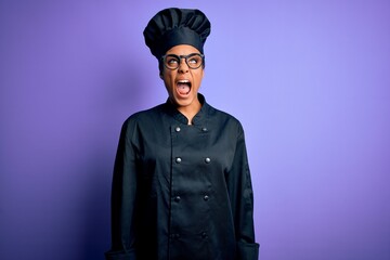 Young african american chef girl wearing cooker uniform and hat over purple background angry and mad screaming frustrated and furious, shouting with anger. Rage and aggressive concept.