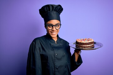 Young african american cooker girl wearing uniform and hat holding tray with cake with a happy face...
