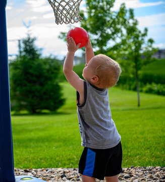 Caucasian Toddler Boy Trying To Dunk On A Small Toy Hoop